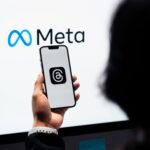 Hands holding smartphone with Meta Threads logo on screen, Meta branding in background.
